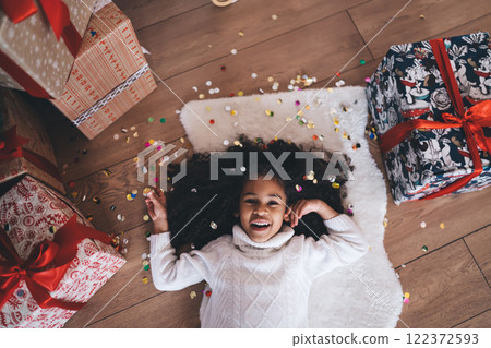 Excited black little girl lying on floor with gift boxes and colorful confetti 122372593