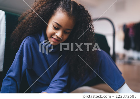 Smiling black girl looking down while playing in room Smiling black girl looking down while playing in room 122372595