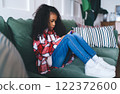 Cute black girl sitting on sofa while browsing smartphone 122372600