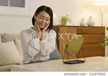 一名50多歲的女性晚上在客廳做皮膚護理 122373630