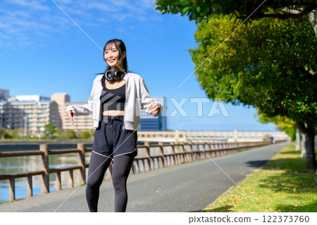 一個很酷的女人在河邊的人行道上伸展她的手臂和腿，散步，節食，散步，運動。 122373760