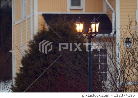 A lit street lamp by a cozy house adds warmth, charm, and elegance to the evening 122374180