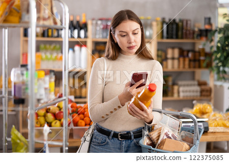 Girl customer holds bottle of peach juice in hand, scans QR code on product label Girl customer holds bottle of peach juice in hand, scans QR code on product label 122375085