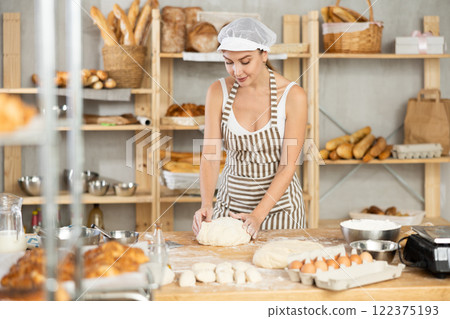 Female baker stands at his work bench, kneading and shaping dough to make bread, croissants and baguettes 122375193