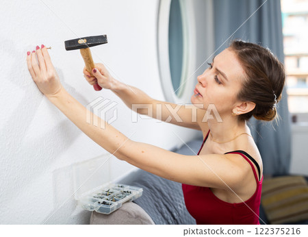 Woman using hammer to drive nail into wall Woman using hammer to drive nail into wall 122375216