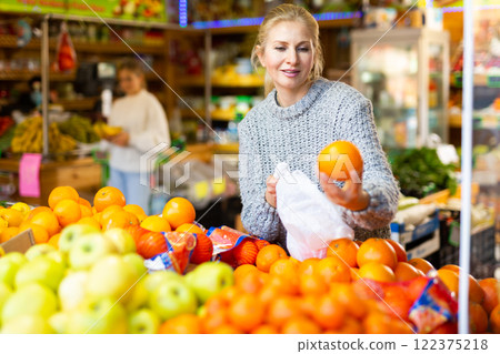 Smiling woman choosing sweet ripe oranges in farmer store 122375218
