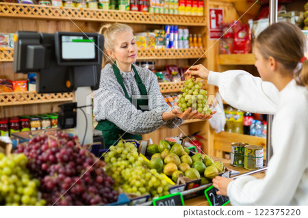 Saleswoman taking grape from female customer for weighing in grocery 122375220