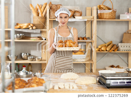 Smiling female baker presenting freshly baked croissants 122375269