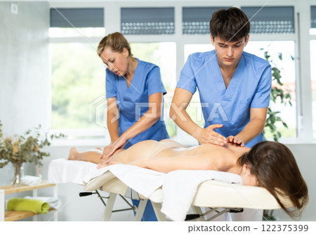 Professional masseur and masseuse performing back massage for female patient Professional masseur and masseuse performing back massage for female patient 122375399