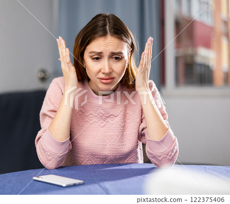 Portrait of a frustrated young woman sitting at a table Portrait of a frustrated young woman sitting at a table 122375406