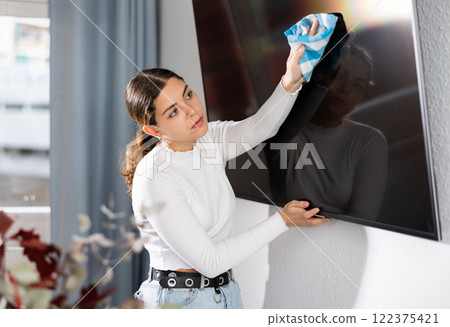 Woman cleaning TV screen in living room 122375421