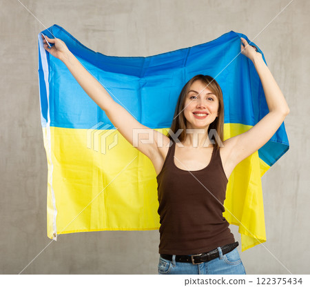 Portrait of confident smiling young female student standing against gray wall with national flag of Ukraine Portrait of confident smiling young female student standing against gray wall with national flag of Ukraine 122375434