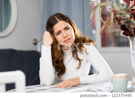 Upset woman sitting at table at home Upset woman sitting at table at home 122375495