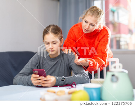 Daughter plays on smartphone while mother tries to talk to her Daughter plays on smartphone while mother tries to talk to her 122375706