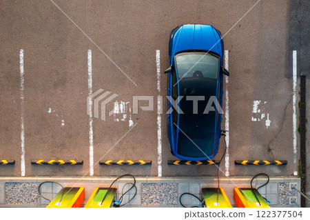 At the parking lot, a blue electric car connects to a charging outlet for electricity. 122377504