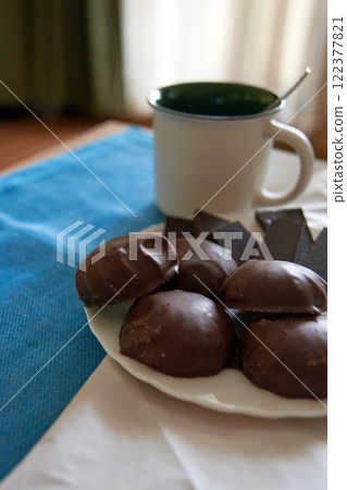 Chocolate-covered marshmallow on a plate on white and blue background. White tea cup in defocus Chocolate-covered marshmallow on a plate on white and blue background. White tea cup in defocus 122377821
