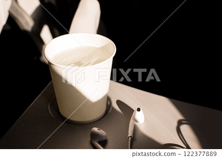 White paper cup of water and headphones on a folding table in an airplane. Drinks on the plane. Dehydration in flight. skin hydration White paper cup of water and headphones on a folding table in an airplane. Drinks on the plane. Dehydration in flight. skin hydration 122377889