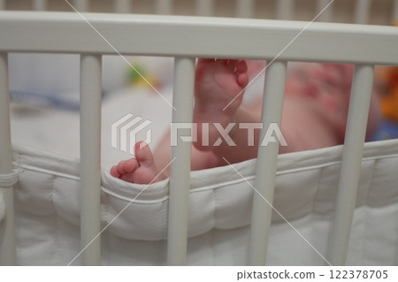 Baby's foot hangs from a white bed Baby's foot hangs from a white bed 122378705
