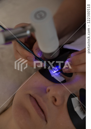 A woman undergoing eyelash extension procedure using an ultraviolet lamp. A woman undergoing eyelash extension procedure using an ultraviolet lamp. 122380518