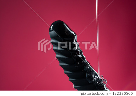 Lube pouring on black dildo on pink background.  122380560