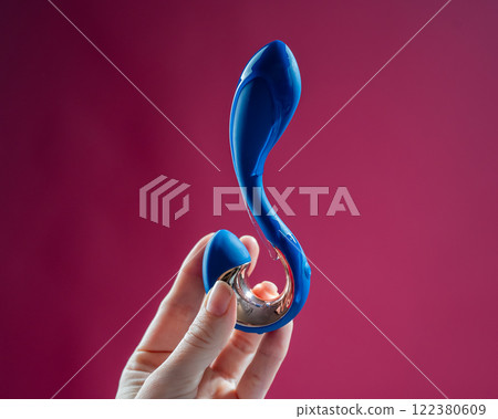 Lube pouring onto blue sex toy on pink background.  122380609
