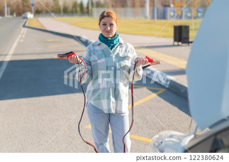 Woman holding clamps for charging a car battery. Woman holding clamps for charging a car battery. 122380624