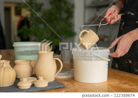 Close-up of a potter's hands glazing a ceramic mug.  122380674