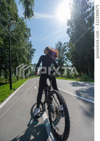 Rear view of Caucasian woman riding bike in park. Vertical photo.  122380675