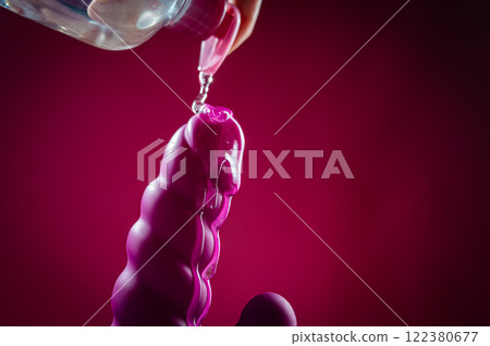 Lube pouring on pink dildo on pink background.  122380677