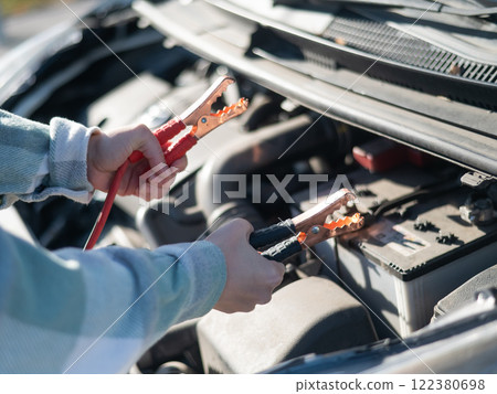 Woman holding clamps for charging a car battery.  122380698