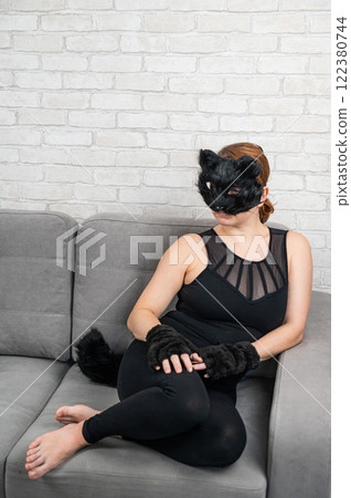 Caucasian woman in cat costume sits on gray sofa. Quadrober. Caucasian woman in cat costume sits on gray sofa. Quadrober. 122380744