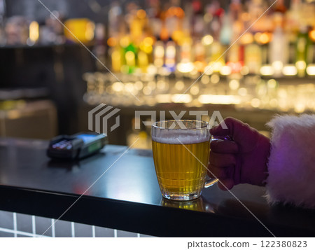Santa Claus drinking beer at a bar. Close-up of a hand holding a mug of beer. Santa Claus drinking beer at a bar. Close-up of a hand holding a mug of beer. 122380823