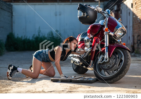 Brunette woman in denim shorts repairs a red motorcycle.  122380903