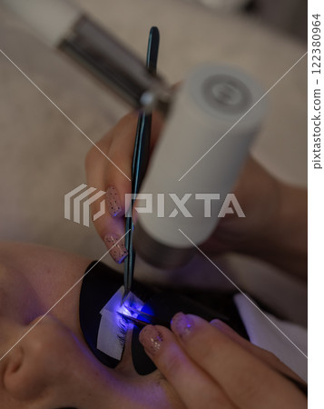 A woman undergoing eyelash extension procedure using an ultraviolet lamp. 122380964