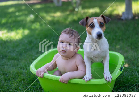 Cute boy bathes in a basin with a Jack Russell terrier dog outdoors in the summer. Cute boy bathes in a basin with a Jack Russell terrier dog outdoors in the summer. 122381058