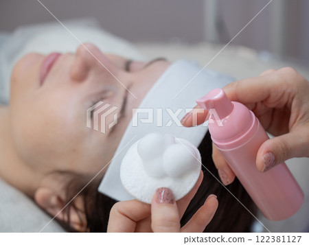 A professional applies cleansing foam to a cotton pad in a beauty salon. A professional applies cleansing foam to a cotton pad in a beauty salon. 122381127