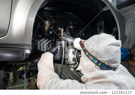 An auto mechanic applies anti-corrosion mastic to the underbody of a car. 122381227