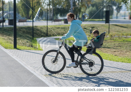 Caucasian woman riding a bicycle with her toddler son sitting behind her in a child seat.  122381233