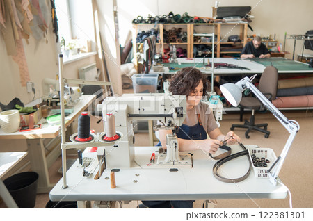 A woman tanner sews a leather belt on a sewing machine. A woman tanner sews a leather belt on a sewing machine. 122381301