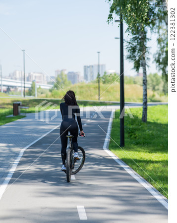 Rear view of Caucasian woman riding bike in park. Vertical photo. Rear view of Caucasian woman riding bike in park. Vertical photo. 122381302