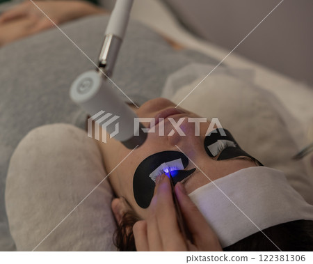 A woman undergoing eyelash extension procedure using an ultraviolet lamp. 122381306