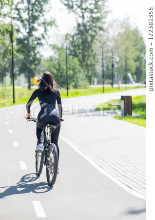 Rear view of Caucasian woman riding bike in park. Vertical photo. Rear view of Caucasian woman riding bike in park. Vertical photo. 122381358