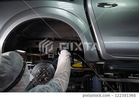 An auto mechanic applies anti-corrosion mastic to the underbody of a car. An auto mechanic applies anti-corrosion mastic to the underbody of a car. 122381368