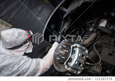 An auto mechanic applies anti-corrosion mastic to the underbody of a car. An auto mechanic applies anti-corrosion mastic to the underbody of a car. 122381378