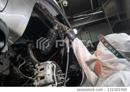 An auto mechanic applies anti-corrosion mastic to the underbody of a car. 122381400