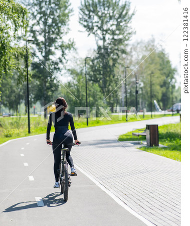 Rear view of Caucasian woman riding bike in park. Vertical photo.  122381416