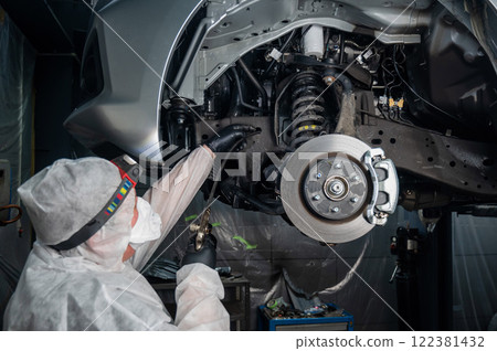 An auto mechanic applies anti-corrosion mastic to the underbody of a car. An auto mechanic applies anti-corrosion mastic to the underbody of a car. 122381432