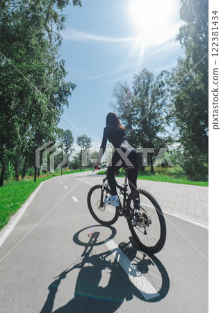 Rear view of Caucasian woman riding bike in park. Vertical photo.  122381434