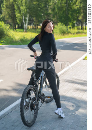 Rear view of Caucasian woman riding bike in park. Vertical photo. Rear view of Caucasian woman riding bike in park. Vertical photo. 122381510