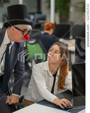 Caucasian woman communicates with an elderly man in a clown costume in the office. Vertical photo. Caucasian woman communicates with an elderly man in a clown costume in the office. Vertical photo. 122381531